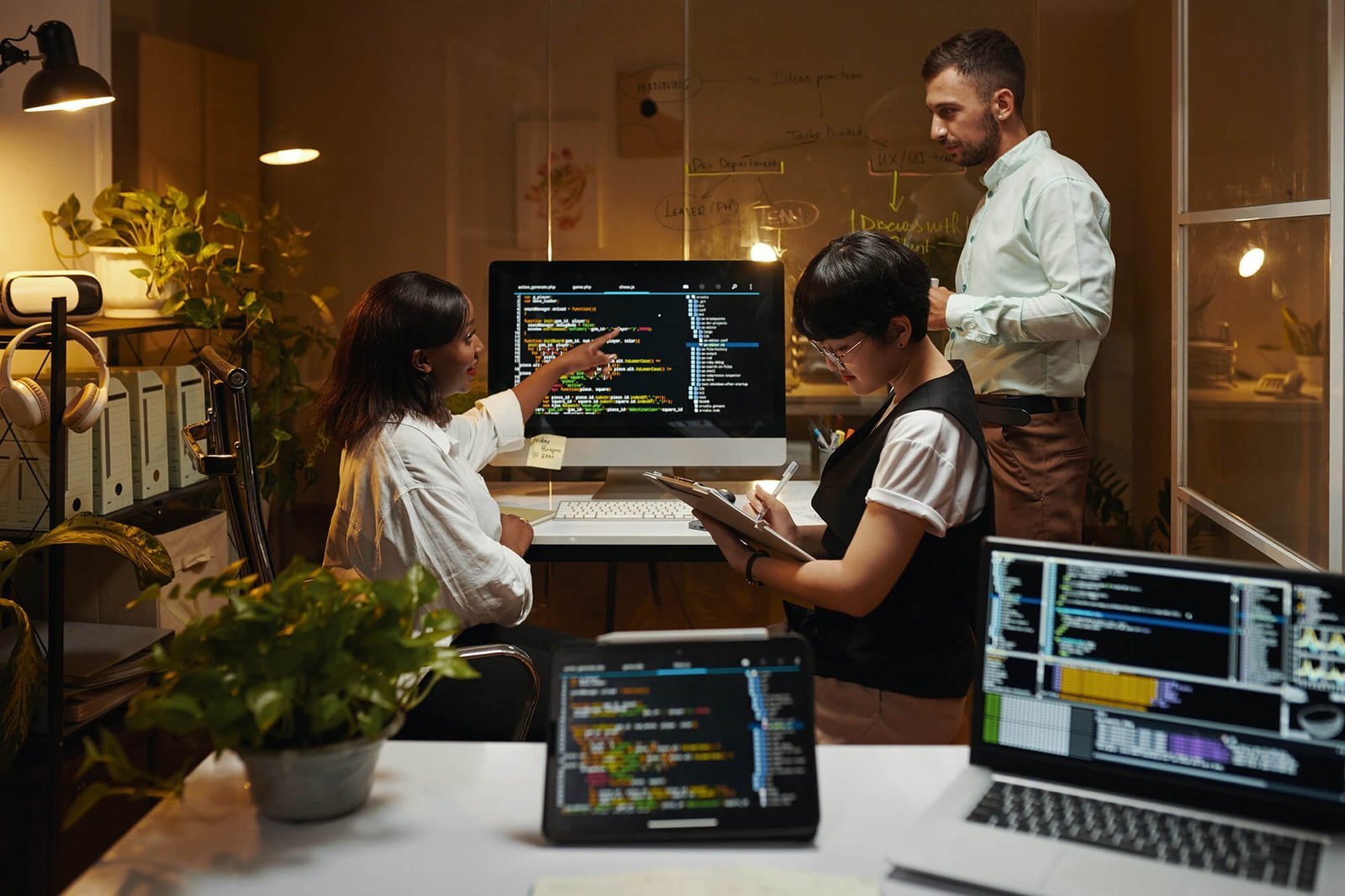 Trois personnes en séance de travail devant un écran affichant du code informatique